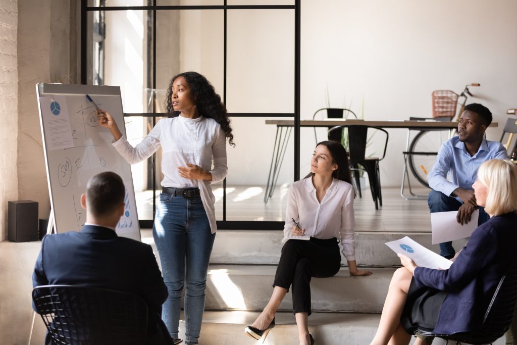 Businesswoman gives presentation using a whiteboard to members of office team.