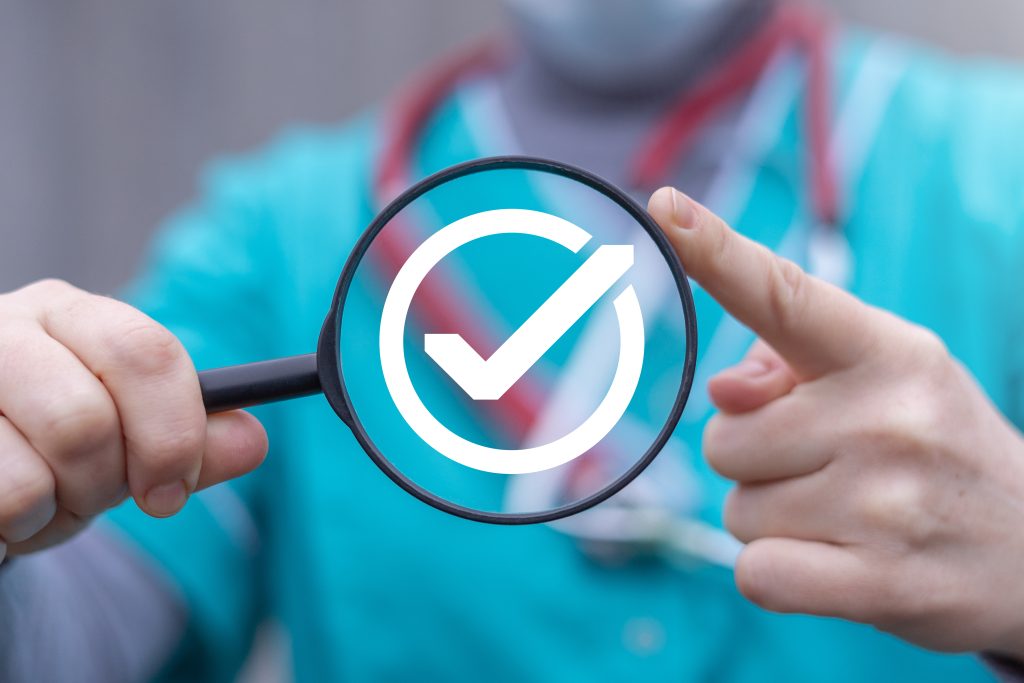 Doctor holds magnifying glass with checkmark on it.